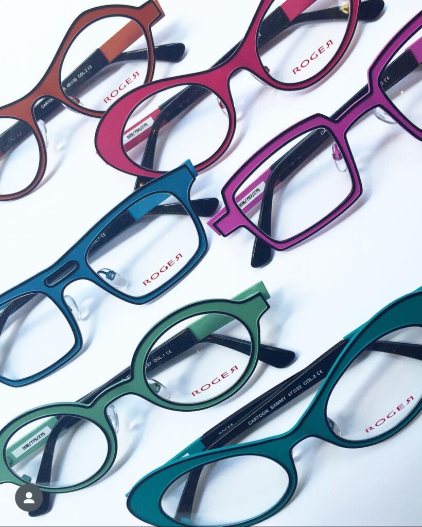 A collection of six colorful pairs of eyeglasses arranged on a white background. The frames are in pink, brown, blue, teal, and green, each with varying shapes and the brand name "ROCCO" visible on the lenses.