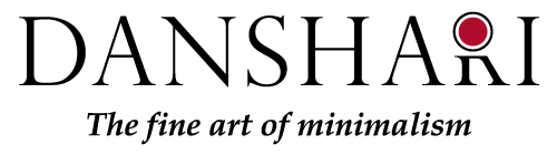 Logo displaying the word "DANSHARI" in bold letters with a red dot inside the letter "A." Below, in smaller cursive text, it reads "The fine art of minimalism." The design is simple and elegant, emphasizing minimalism.