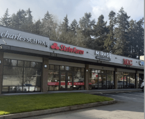 A strip mall with storefronts for Charles Schwab, State Farm, Mirage Optics & Eyewear, and MIC. The buildings are surrounded by trees and the parking lot is in front.